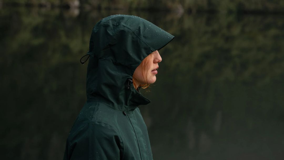 One woman wearing a green raincoat in the rain.